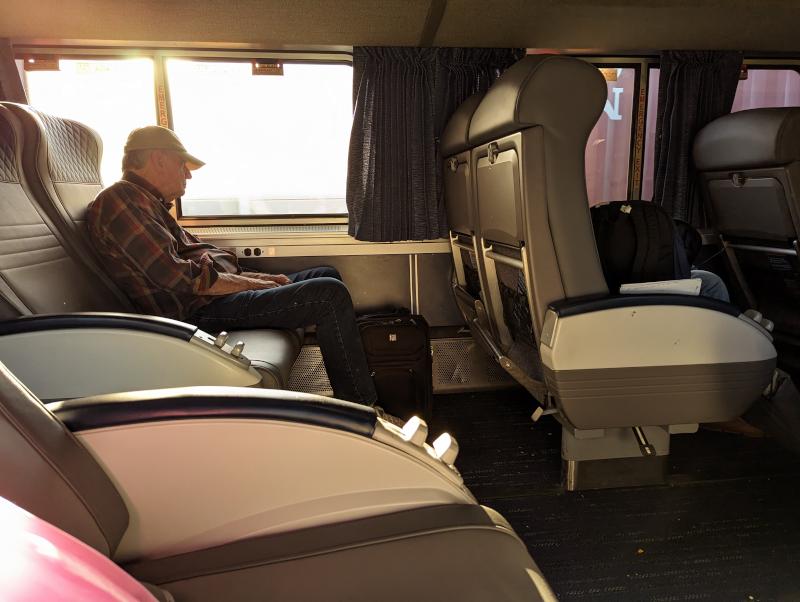 A man sitting in a coach seat, with about 4 feet of space from his knees to the back of the chair in front of him