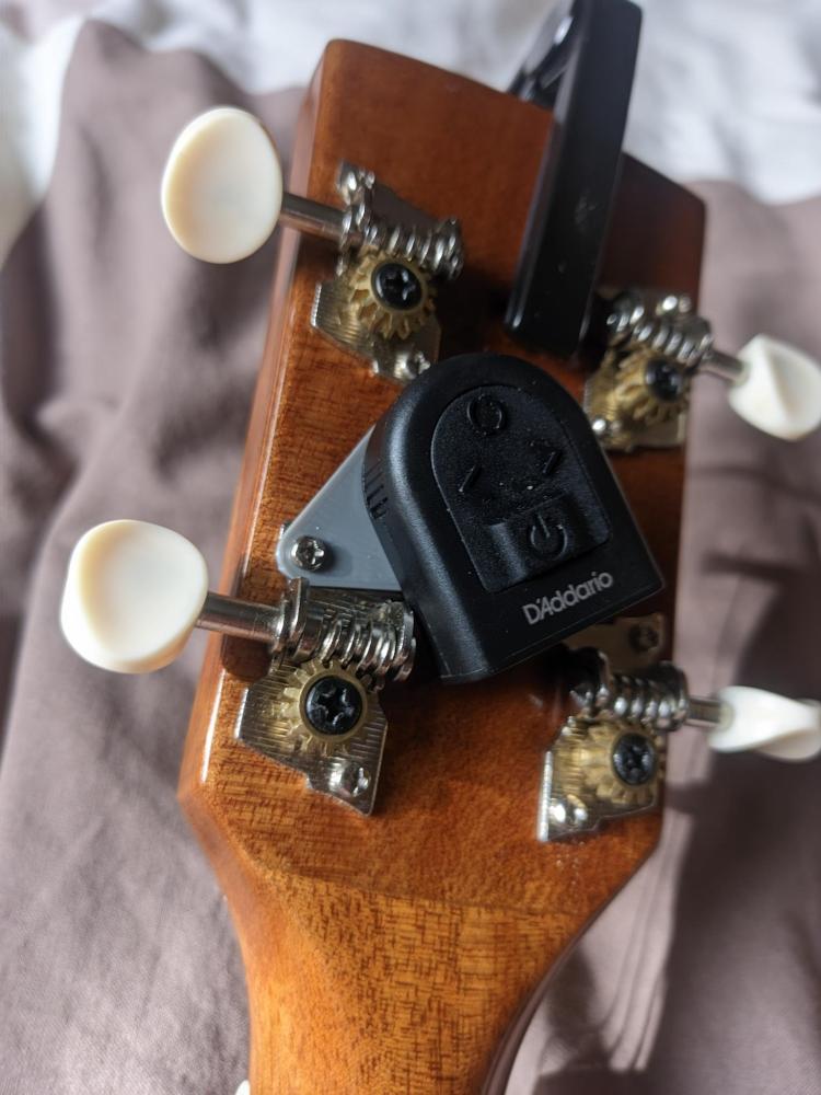 A plastic plate that attaches a small guitar clip to the tuning machine
